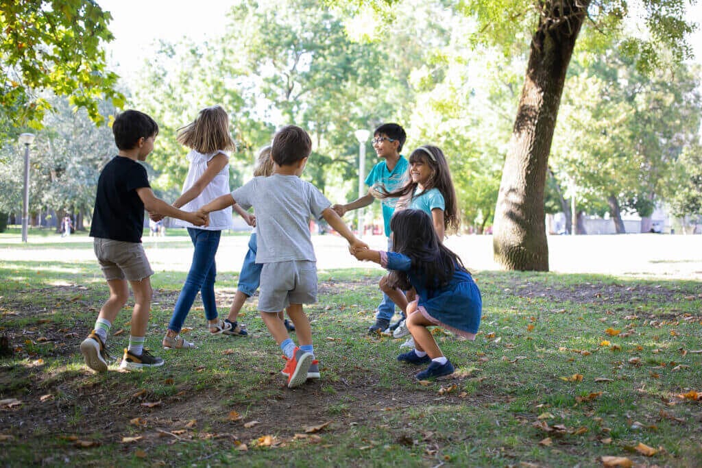 happy children playing together outdoors dancing around grass enjoying outdoor activities having fun park kids party friendship concept